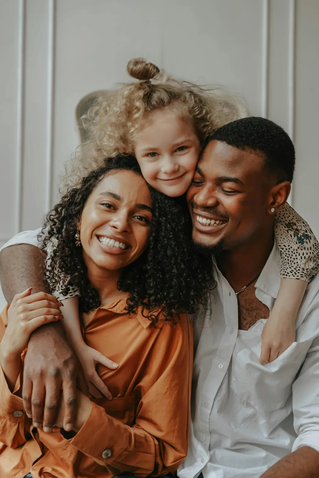 A couple laughing with their young child who is leaning over them from behind, a warm family moment at home