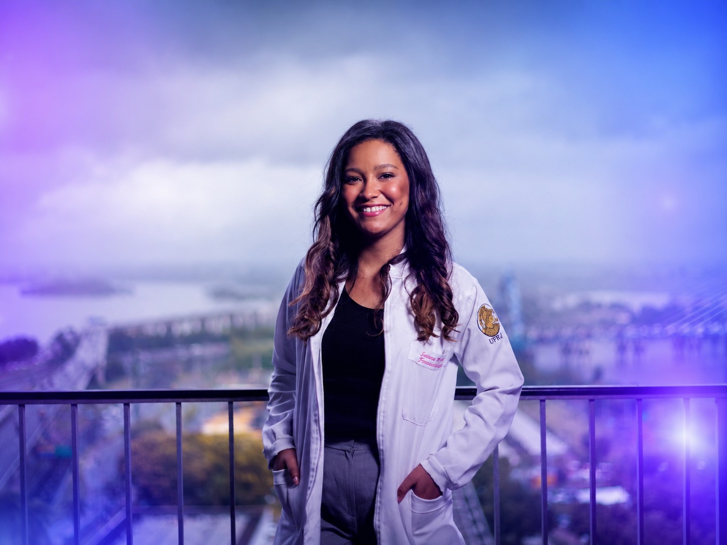 An experienced nurse in a white coat standing confidently on a rooftop balcony overlooking a city.